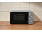A silver microwave oven with a black door on a wooden countertop against a tiled wall.