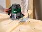 A person uses a router to work on a wooden board on a workbench.