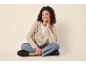 Woman in a beige knitted cardigan, white t-shirt, and jeans, sitting cross-legged.