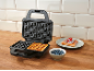 Waffle maker with a waffle, blueberries, and a waffle with strawberries on a plate.