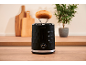 Black toaster with a toasted bun on a rack, on a wooden kitchen counter.