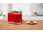 Red toaster with toast and a sandwich on a wooden table in a kitchen.