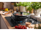 Black pot on a gas stove with tomatoes and herbs cooking in a kitchen.