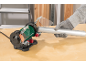 A green and black bench grinder with a person in gloves grinding a metal pipe.