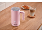 Pink milk frother with illuminated buttons, latte, and croissants on wood.