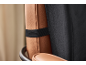 Detail of a brown leather lumbar cushion with a black elastic strap on a chair.