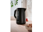 Black electric kettle on a wooden kitchen counter with tea and cookies.