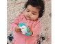 Baby in pink sleepsuit holding a hedgehog teether on a patterned rug
