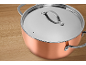 Copper pot with a stainless steel lid and handles on a wooden surface