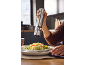 Hand seasoning a couscous dish with an electric pepper grinder.