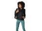 Smiling woman in black jacket and aqua sports leggings, with a gray backpack.