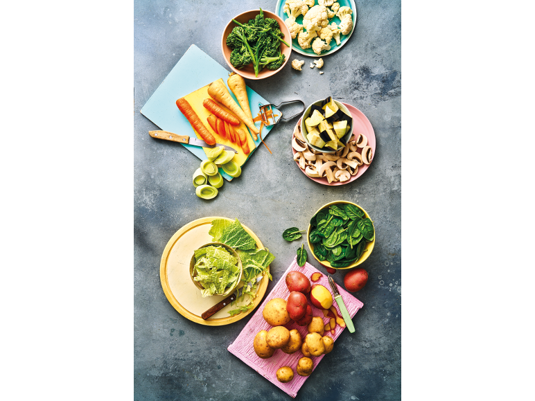 Overhead shot of various fresh vegetables, including carrots, potatoes, broccoli, and spinach, prepared for cooking.