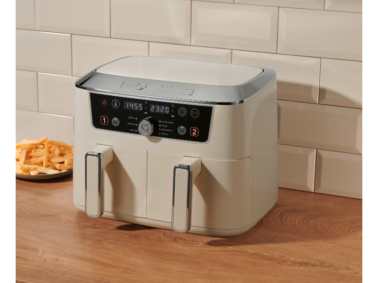 Cream dual-basket air fryer with digital display showing 14:55 and 23:20, next to fries.