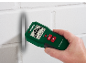 Hand holding a multi-sensor wall scanner detecting a pipe in a white brick wall.