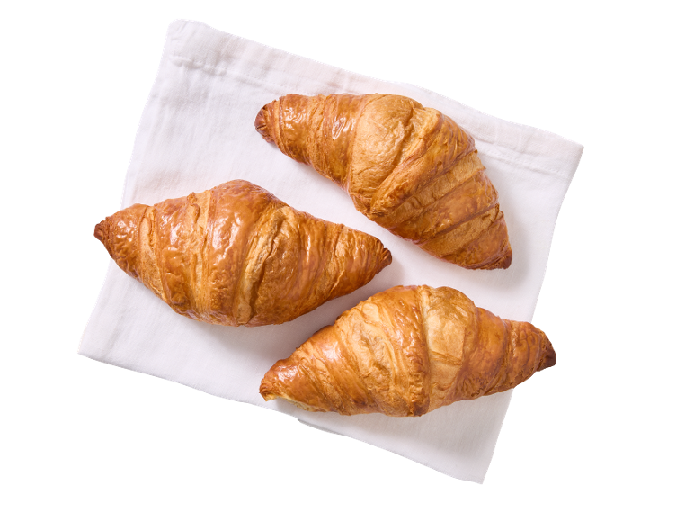 Three golden-brown croissants on a white napkin, viewed from above.
