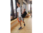 Man in white t-shirt, grey shorts, and sneakers, with a black sports bag and orange towel.