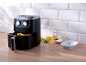 Black air fryer with fries, oil, sauces, and rosemary on a wooden table.