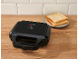 Black sandwich maker on a wooden countertop with toast on a plate.
