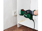 Green multi-tool cutting a white shelf, with sawdust and a wall socket.