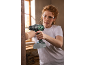 Woman with cordless drill and safety glasses drilling wood, with sawdust flying.