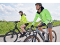Man and woman in bright jackets and helmets riding bikes on a road.