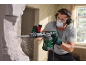 Man using a demolition hammer to break down a wall, wearing protective gear.