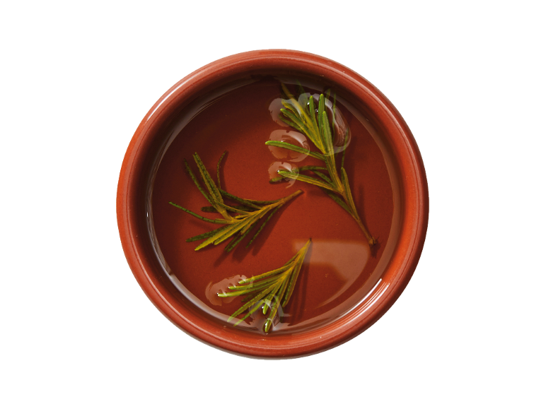 Fresh rosemary sprigs floating in olive oil in a terracotta bowl.