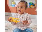 Smiling baby holding a yellow animal-shaped rattle, sitting on a rug.