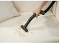 Hand vacuuming crumbs from a light-colored sofa with an attachment.
