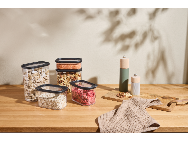On a kitchen counter, transparent storage containers with cereals, nuts, and dried fruit, and spice grinders.