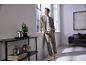 Man in khaki tracksuit jacket and trousers, white t-shirt, and beige sneakers, looking out a window.
