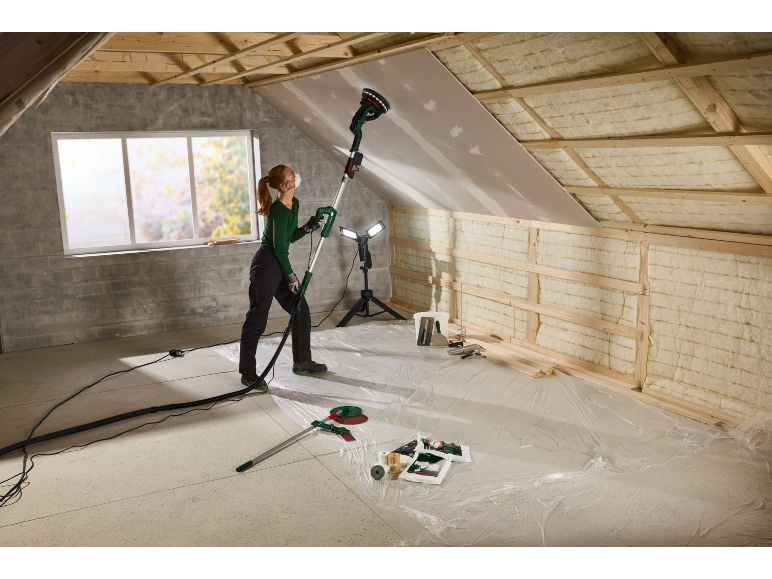 Woman sanding a ceiling with a telescopic sander in an attic under renovation.