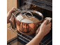 Man in oven mitts placing a pot into the oven.