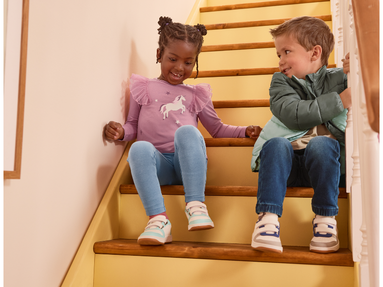 Two children in casual wear and sneakers sitting on wooden stairs, smiling.