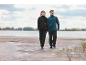 Two people in outdoor jackets and convertible trousers walking on a beach.