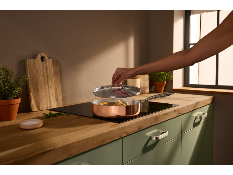 Cooking in a copper pan on an induction hob, with a wooden cutting board and herbs.