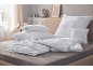 White bedding on a bed, including pillows and a quilted duvet.