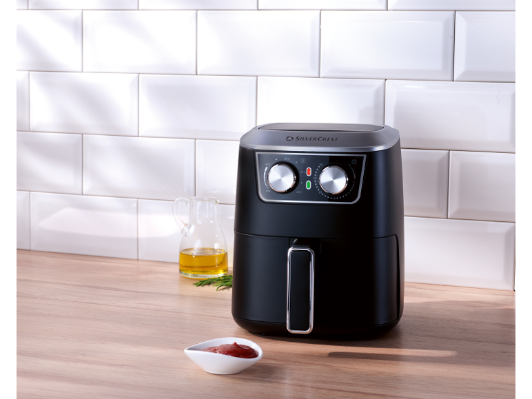 Black air fryer on a wooden counter with an oil jug and ketchup.