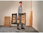 Man carrying a foldable workbench in a room with wooden planks.
