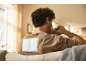 Man with warming patches on his back drinks coffee on the couch.