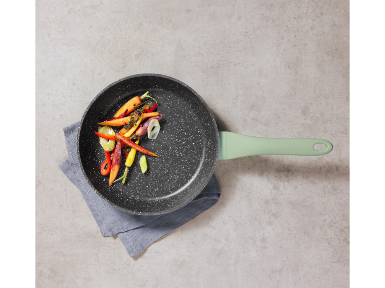 Frying pan with roasted vegetables (carrots, peppers, onion) on a grey cloth.