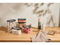 Transparent food containers with dry goods and pepper grinders on a wooden table.