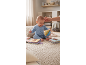 A smiling baby in blue pajamas plays with a fabric ball and soft books on a rug.