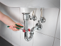 A hand holding pliers tightens a drain pipe under a sink.