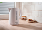 White electric kettle on a wooden countertop with cookies and tiles in the background.