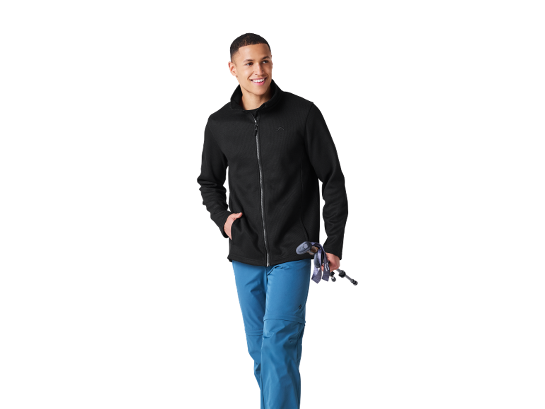 Man in black fleece jacket and blue trousers holding hiking poles.