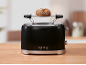 Black toaster with a bread roll on the warming rack, on a wooden countertop.