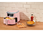 Pink air fryer with fries, sauce, and salt on a wooden kitchen counter.