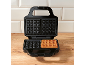 Open waffle maker with one cooked waffle on a wooden countertop.