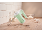 Mint green hand mixer with whisks, milk, flour, and eggs on a wooden countertop.